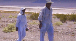 Two people in white clothes walking on a beach.