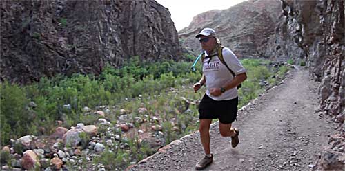 A man is running on the trail in front of some mountains.