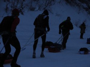 Three people are walking in the snow with a sled.
