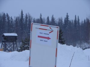 A sign in the snow with directions to ski resorts.