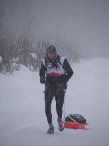 A man in black and white ski suit carrying a red sled.