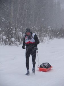 A man is skiing in the snow with his sled.