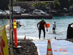 A man in black wetsuit standing on water near orange cones.