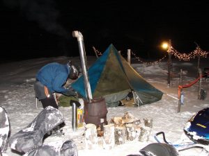 A man standing next to a tent in the snow.