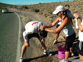 A woman helping another man climb up the side of a road.