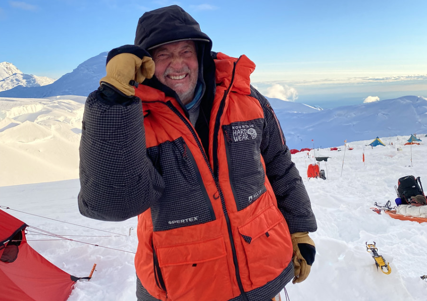 A man in an orange and black jacket on top of a mountain.